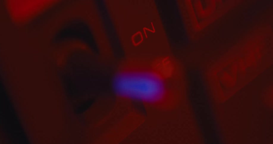 Red light shines as a persons finger flips a switch on a device and the reflection of a blue light is seen on the switch