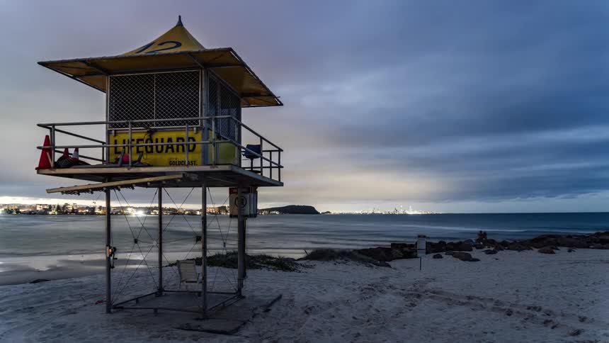 Time lapse of a lifeguard tower in front of a beach close to a small coastal town