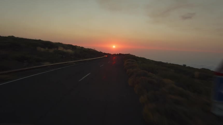 A road along a hill overlooking the ocean at sunset