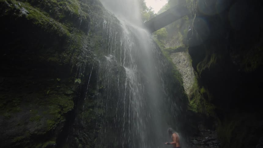 Water flows down a sheer rock face and showers onto a man standing in the ravine