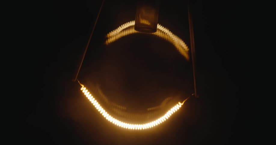 Close up of a lightbulb filament turning on inside a dark room