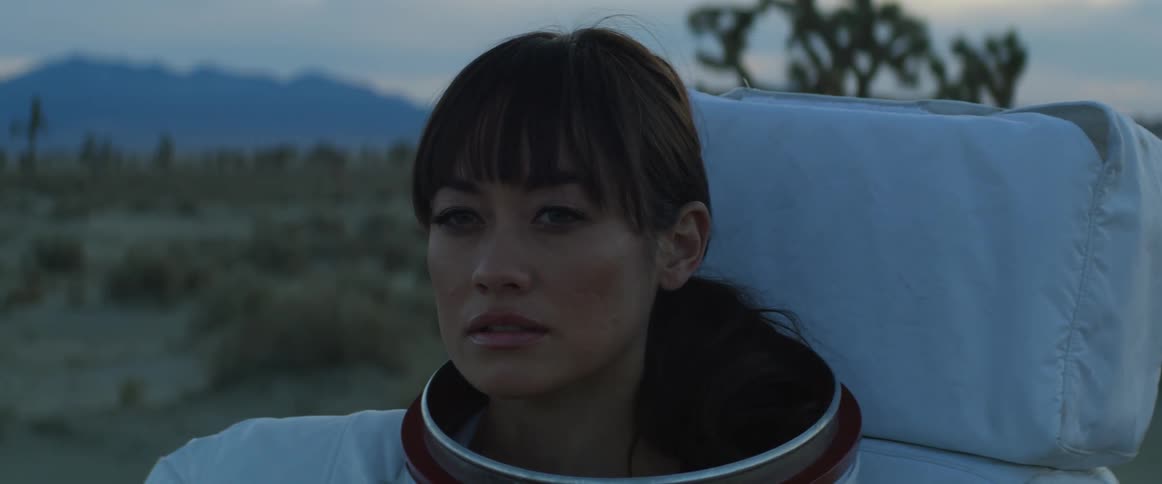 A woman in an astronaut suit stands on the land and looks around