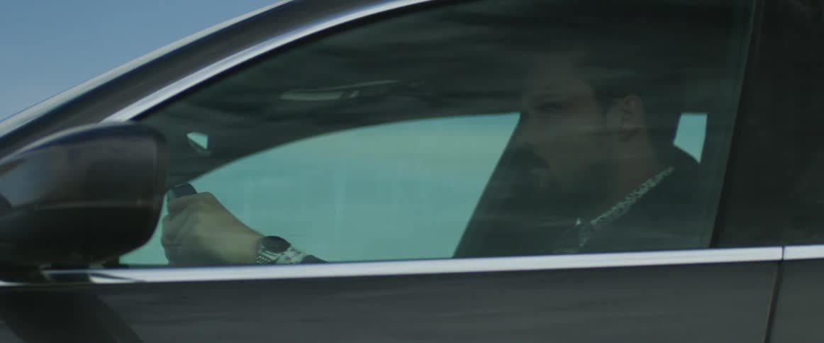 Man wearing elegant clothes drives a dark grey car at daytime