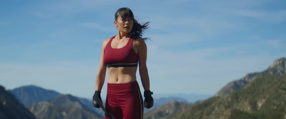 A woman is breathing hard as she stretches her arm and shoulder while standing on a mountain