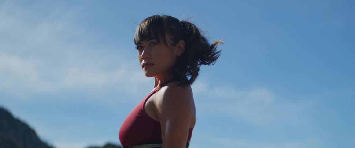 A woman in workout clothes is standing in the mountains breathing and sweating