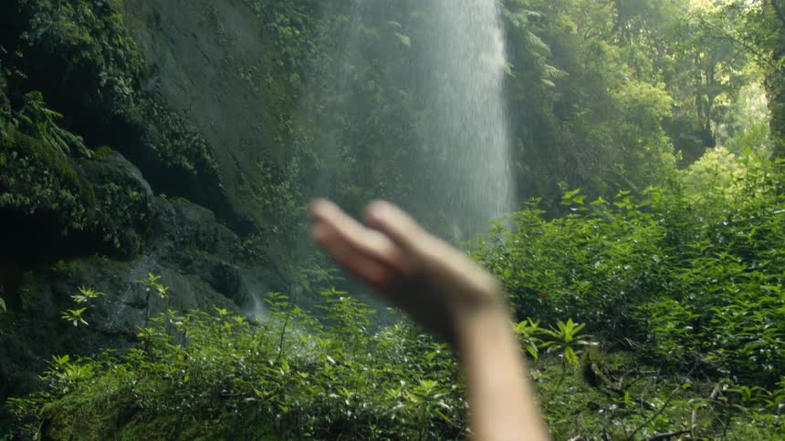 A woman holding her hand up moving it around to feel the mist from the flowing waterfall