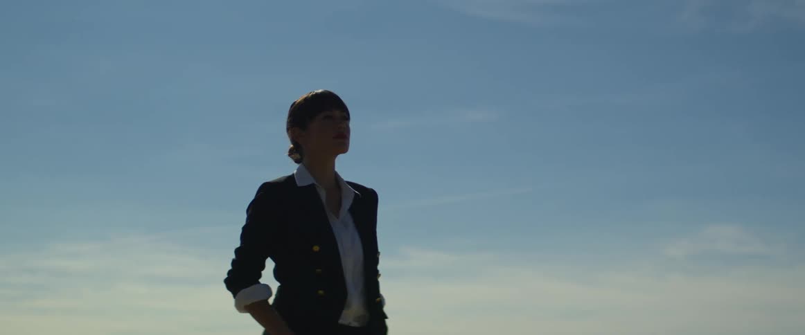 Woman with a bun and suit stands on mountain looking into space