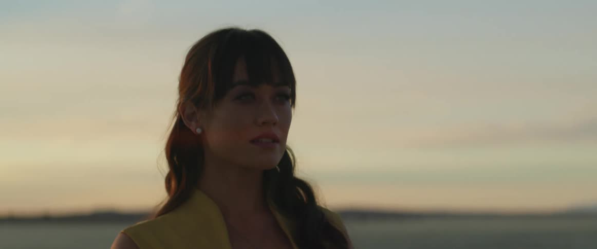 A woman is standing outdoors while the sun is setting