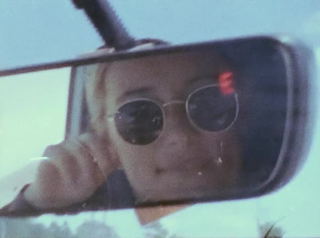 The rearview mirror reflects the smiling face of the woman driving the car