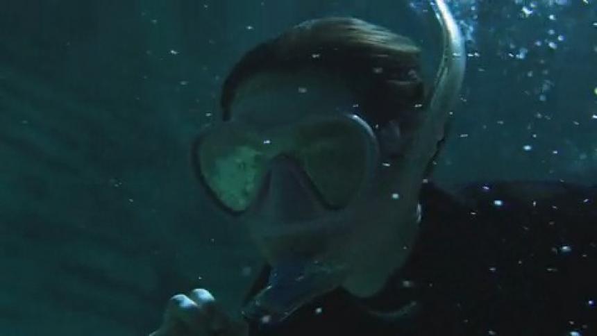 Woman free diving in cave descends with flashlight