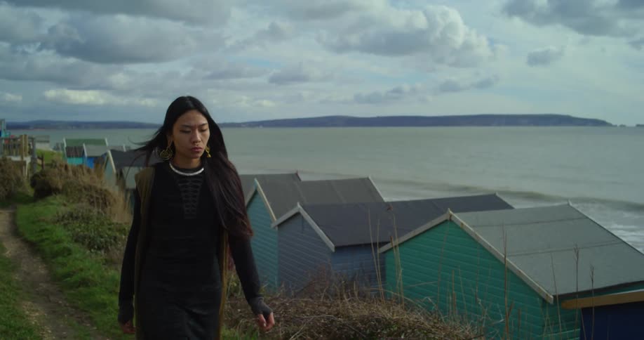 A woman walks past beach huts overlooking the sea