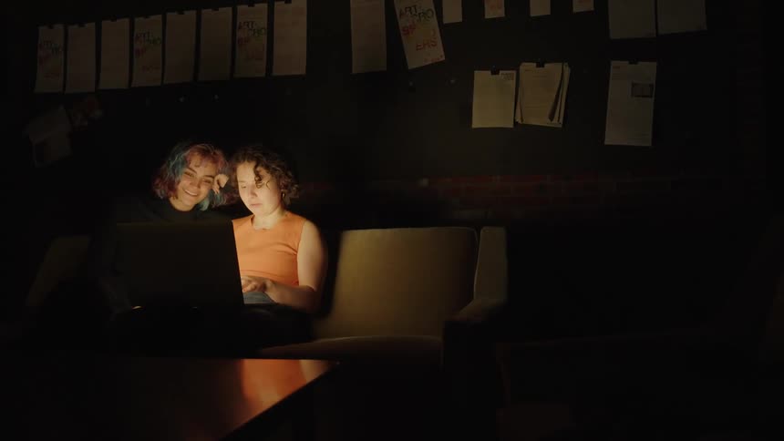 Two girls type on a computer in a dark room