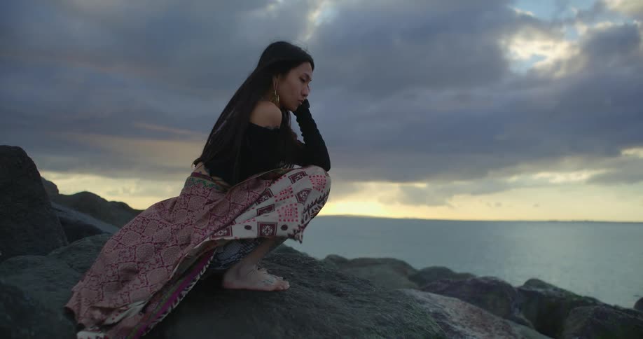 A woman crouches on rocks by the sea