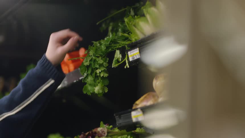 Person with long sleeves picks bunch or parsley from the produce shelf