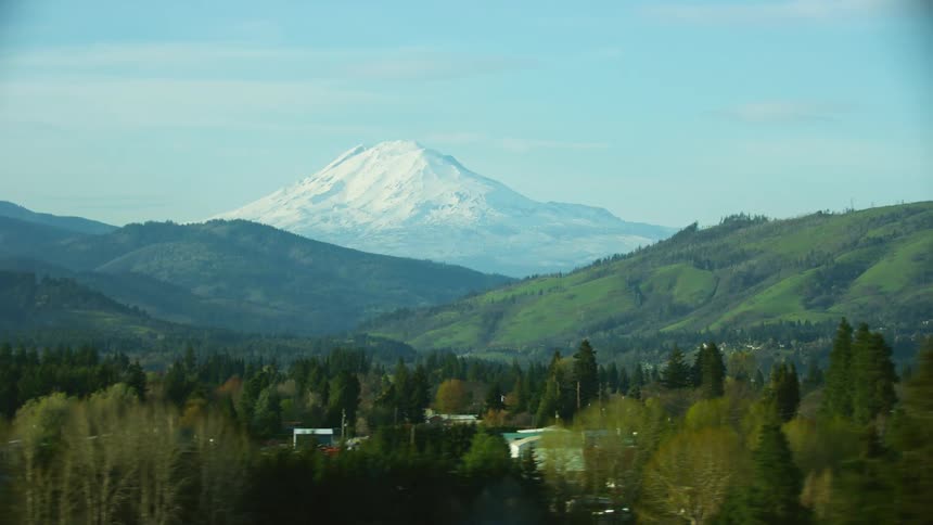 A large snow covered volcano towers over other mountains and a town