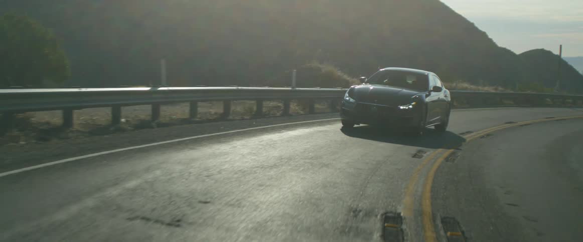 Car travels on a curved road near the mountains on a sunny day