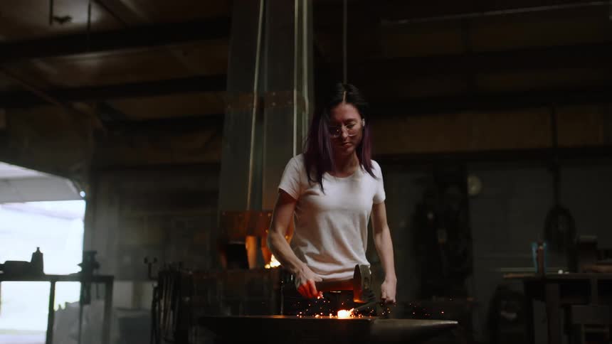 A woman hammering heated metal in a workshop