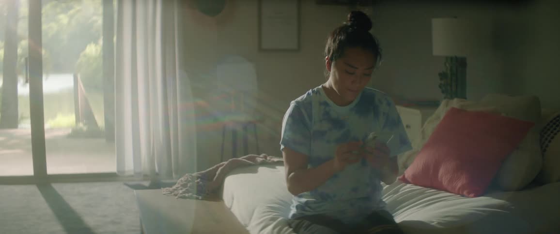 A teenager scrolls through her smartphone while sitting on her bed