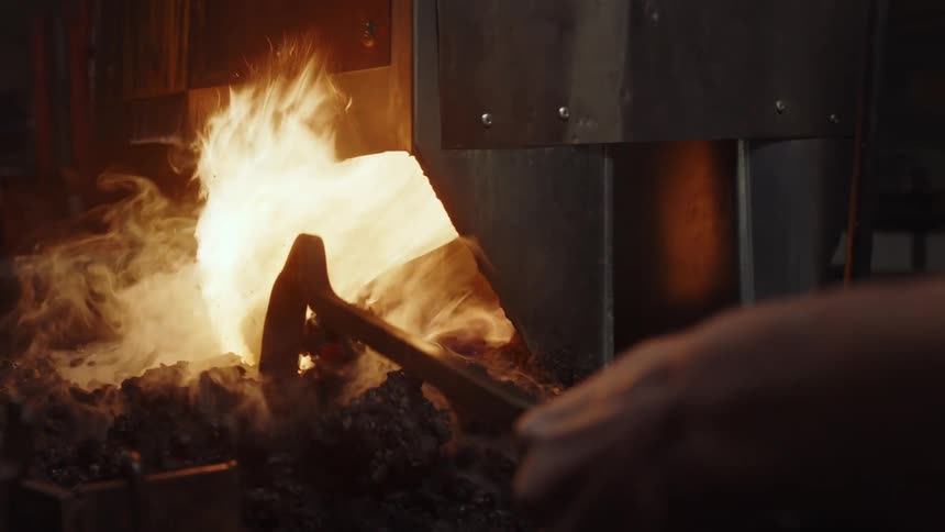 A man uses a metal rod to break up fire ash in a kiln