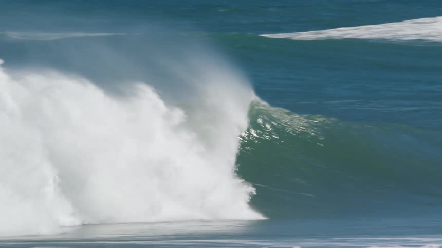 Surfer wearing red wetsuit paddles and rides wave on surfboard