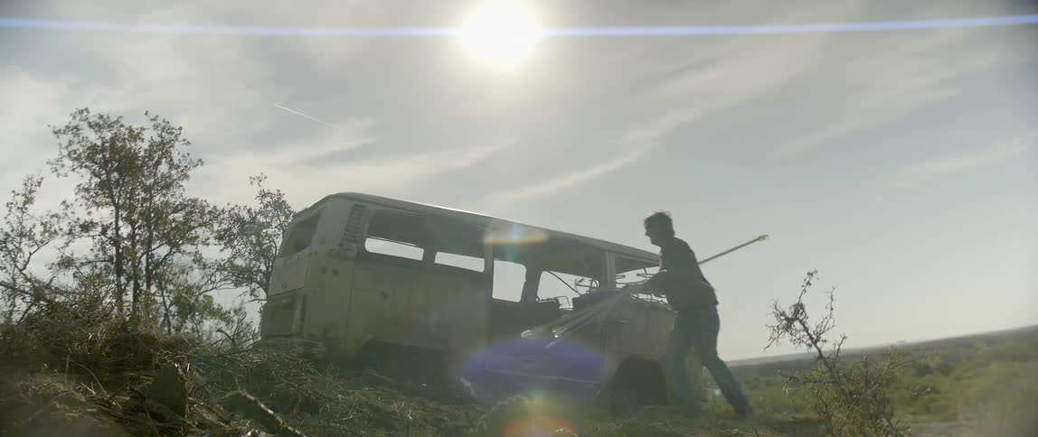 A man carries some objects and puts them in an abandoned van