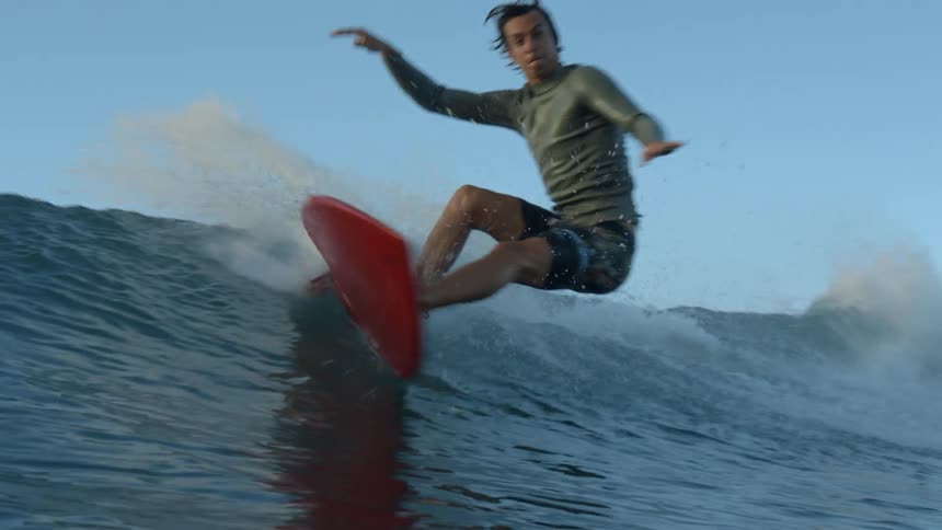 Man with wetsuit rides on waves on a surfboard at sunset