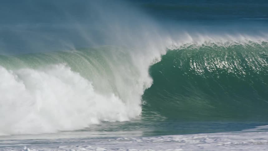 A surfer catches a large wave while others wait for the next one