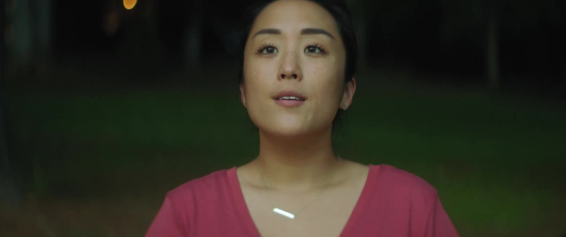 Woman with necklace and pink blouse raises her head and looks up smiling