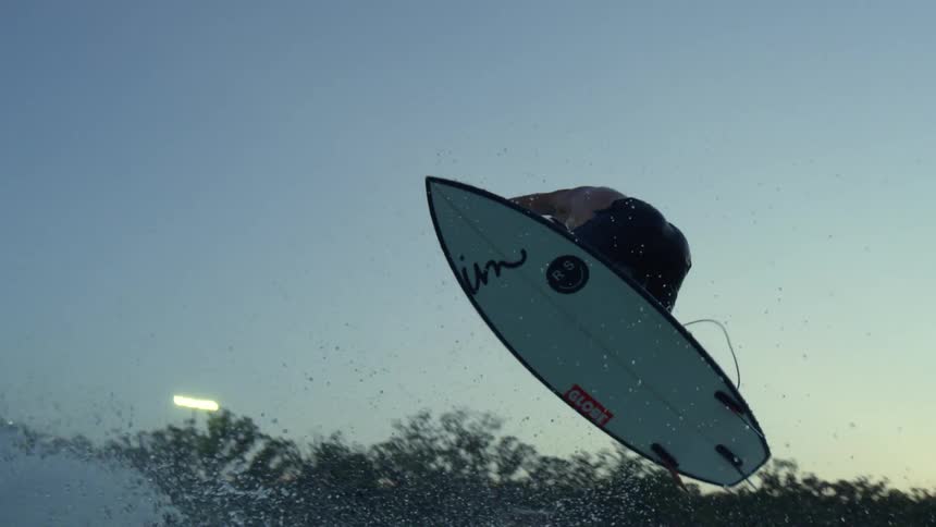 Man surfs over an ocean wave then goes airborne and spins around then lands on the surface of the water