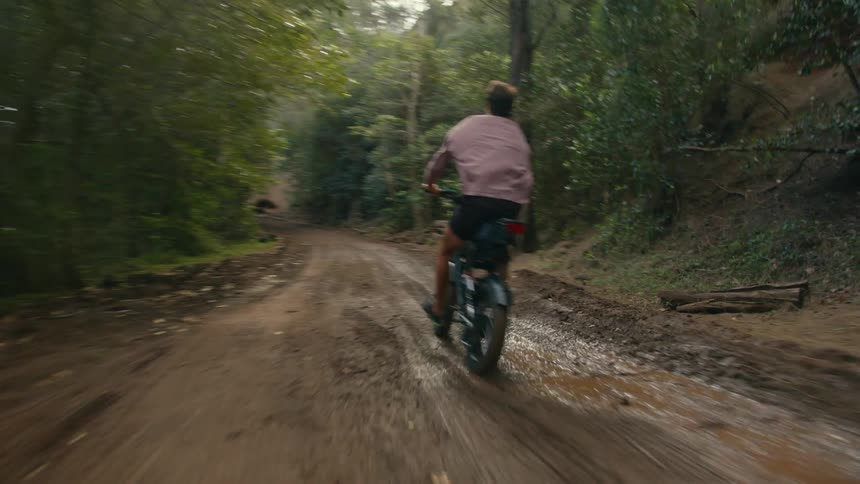 Man wearing shorts rides a bike on a muddy dirt trail in the forest