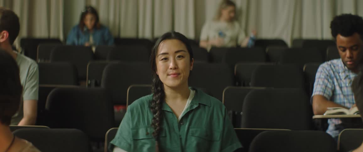 A young woman looks happy and confident smiling as students are seated in a university auditorium