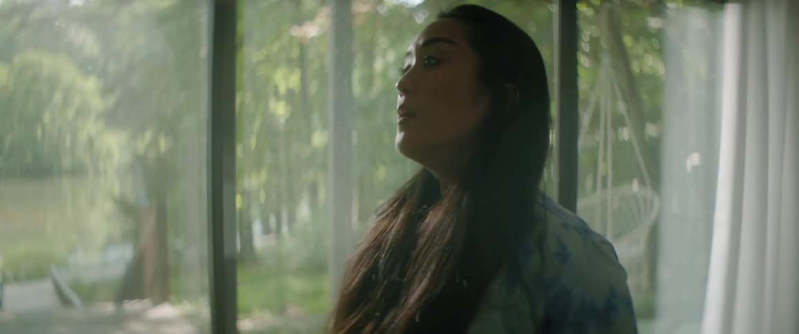 Woman stands next to a window and runs her fingers through her long hair
