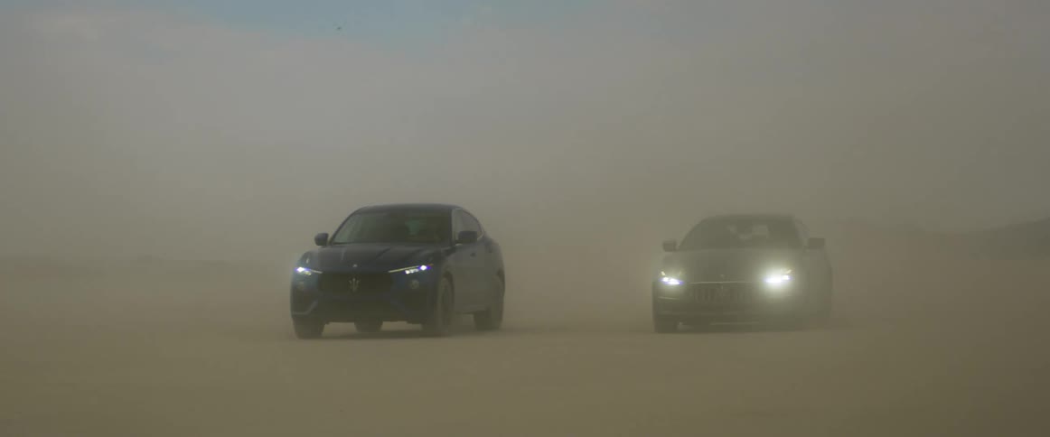 Two cars drive through a dust cloud
