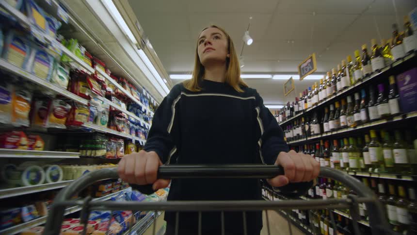 A customer walking through a grocery store with a cart