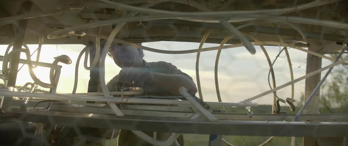 An older man works on some tubing in some farm machinery