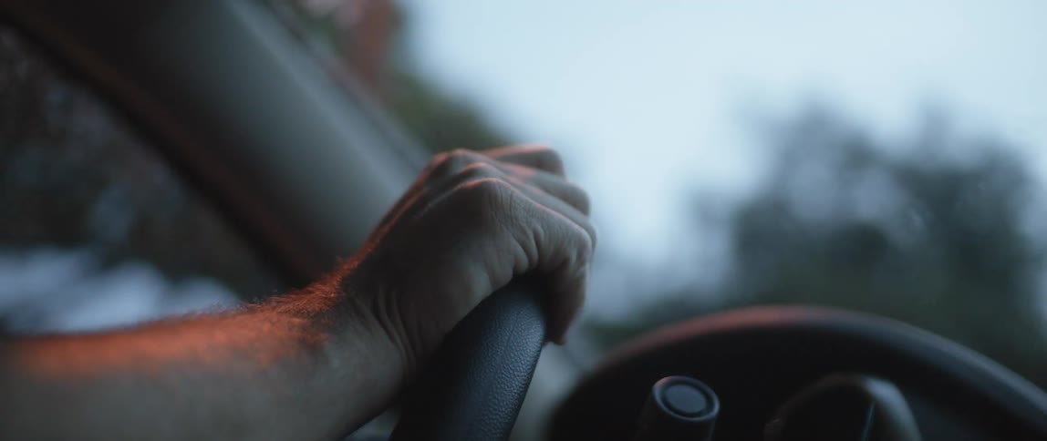 Close up of a mans hand as he holds a steering wheel while driving in the rain