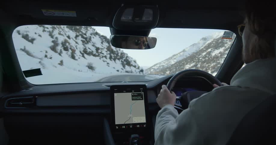 A man is driving an automobile on a snow covered mountain road and there is a gps on the dashboard