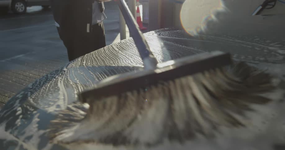 A man brushes soap on the front of his car as he washes it