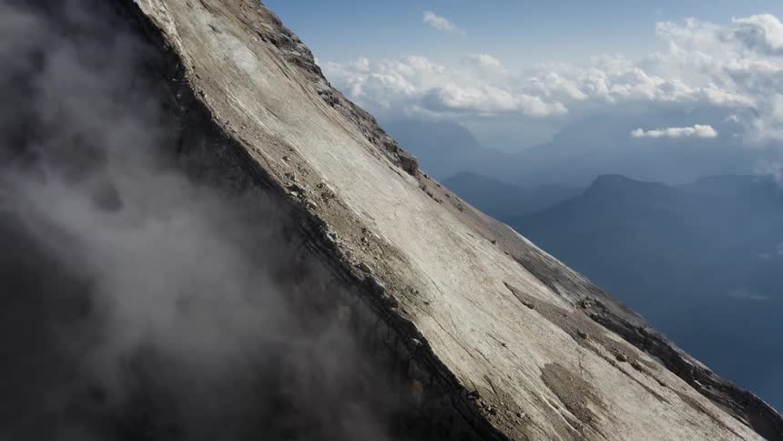 Fog is rising from the side of a mountain and there are silhouettes of mountains in the distance high among the clouds