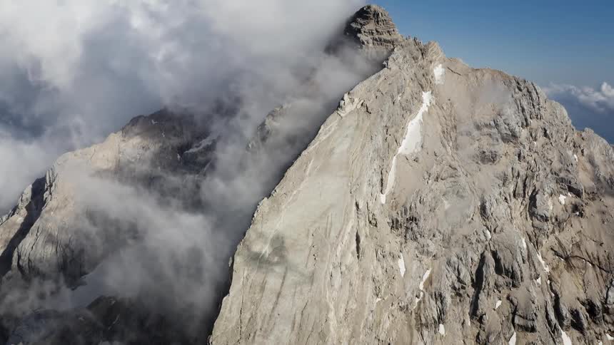 Snow settles in ridges along the side and peak of a tall mountain