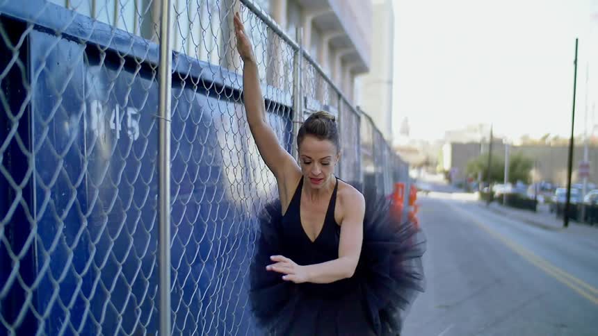A ballerina leaping using a fence as a prop