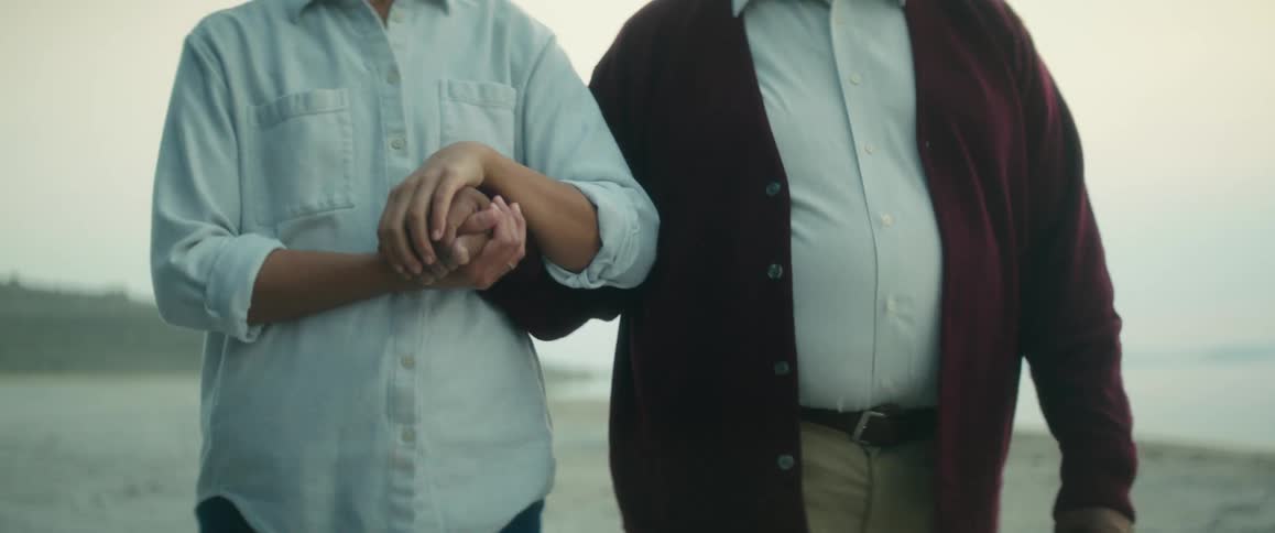 Couple holding hands walking on a beach next to the ocean at evening