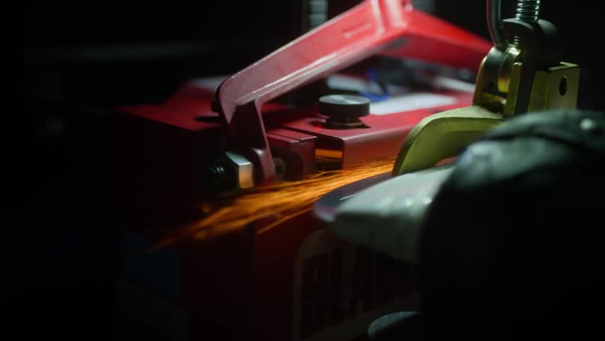 A hand held power saw creates sparks as it is shapes a clamped piece of metal