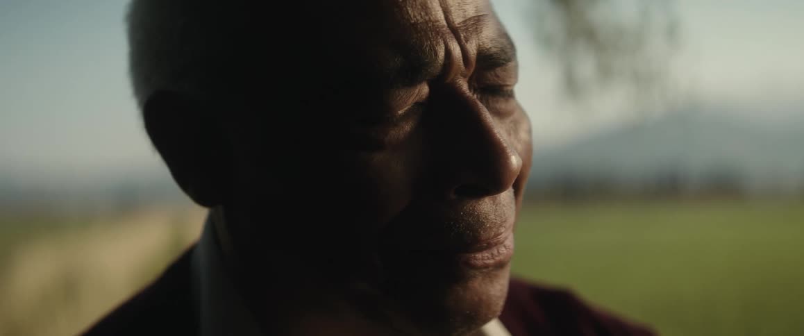 A man smiles to himself while standing with his eyes closed in a field