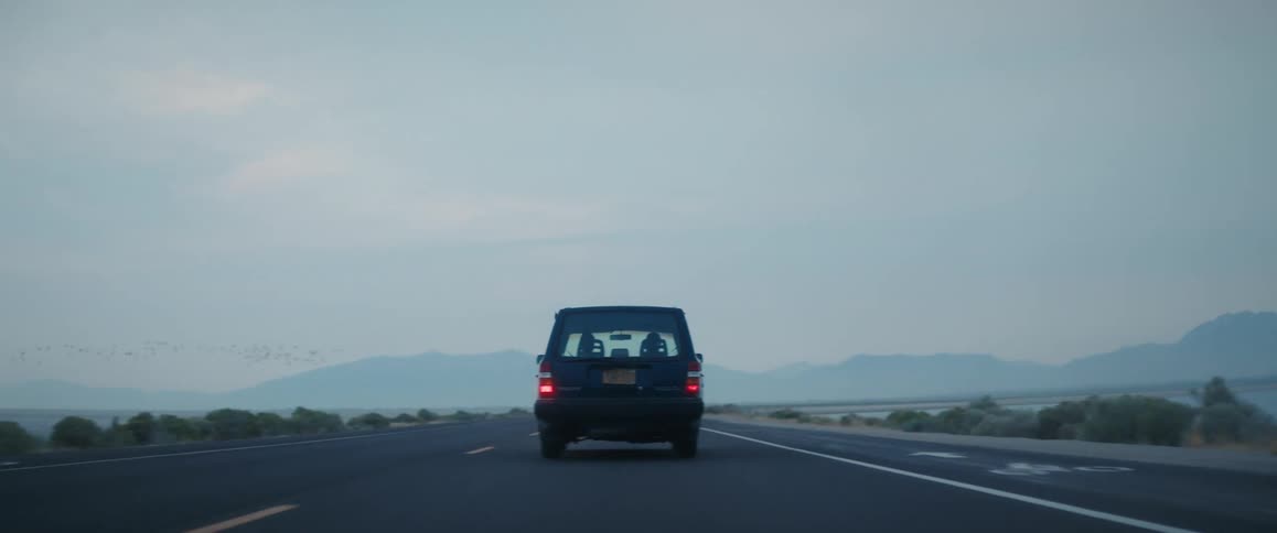 A volvo station wagon travels along a road through the countryside toward distant mountains shrouded in fog