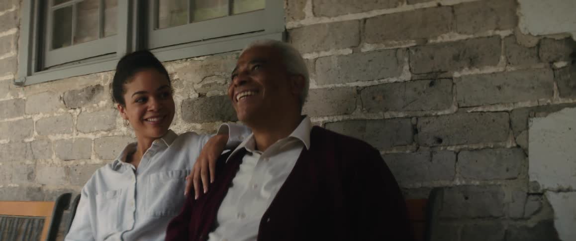 A woman and her grandfather sitting on a porch bench drinking soda from bottles