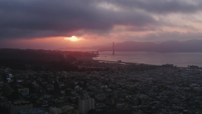 The silhouette of a bridge and hills across the water from a coastal city at sunrise
