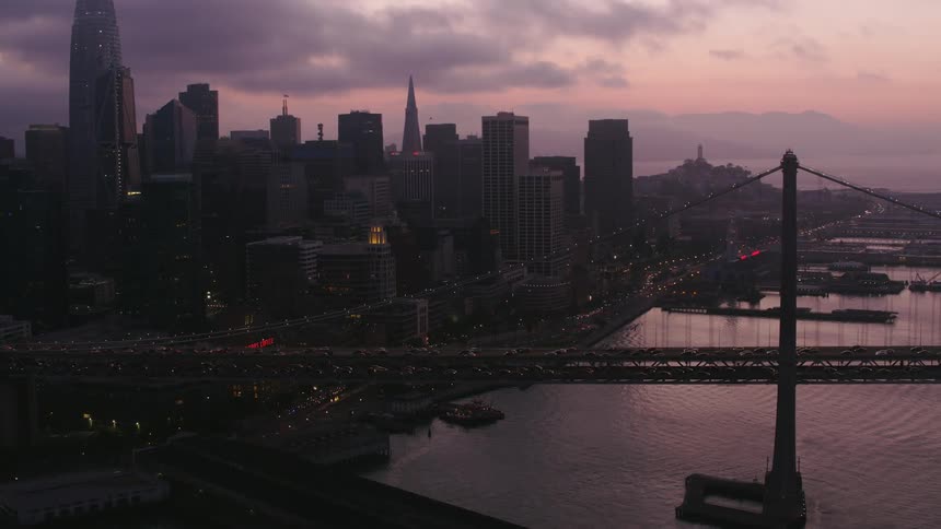 Tall buildings and skyscrapers on the coast of a metropolis as the sun sets on a cloudy day