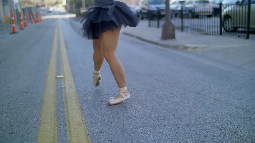 A ballerina dances down the middle of an urban street during the day