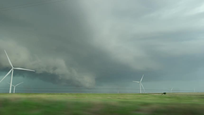 Windmills generate power as they rotate in front of a supercell severe thunderstorm with a rotating base of clouds in rural Oklahoma
